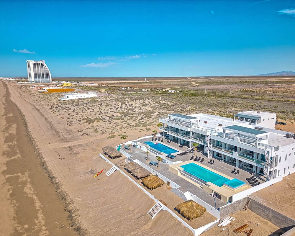 Aerial view of the long sandy beach at Playa Encanto, with Six Palms Villas and their pools in front
